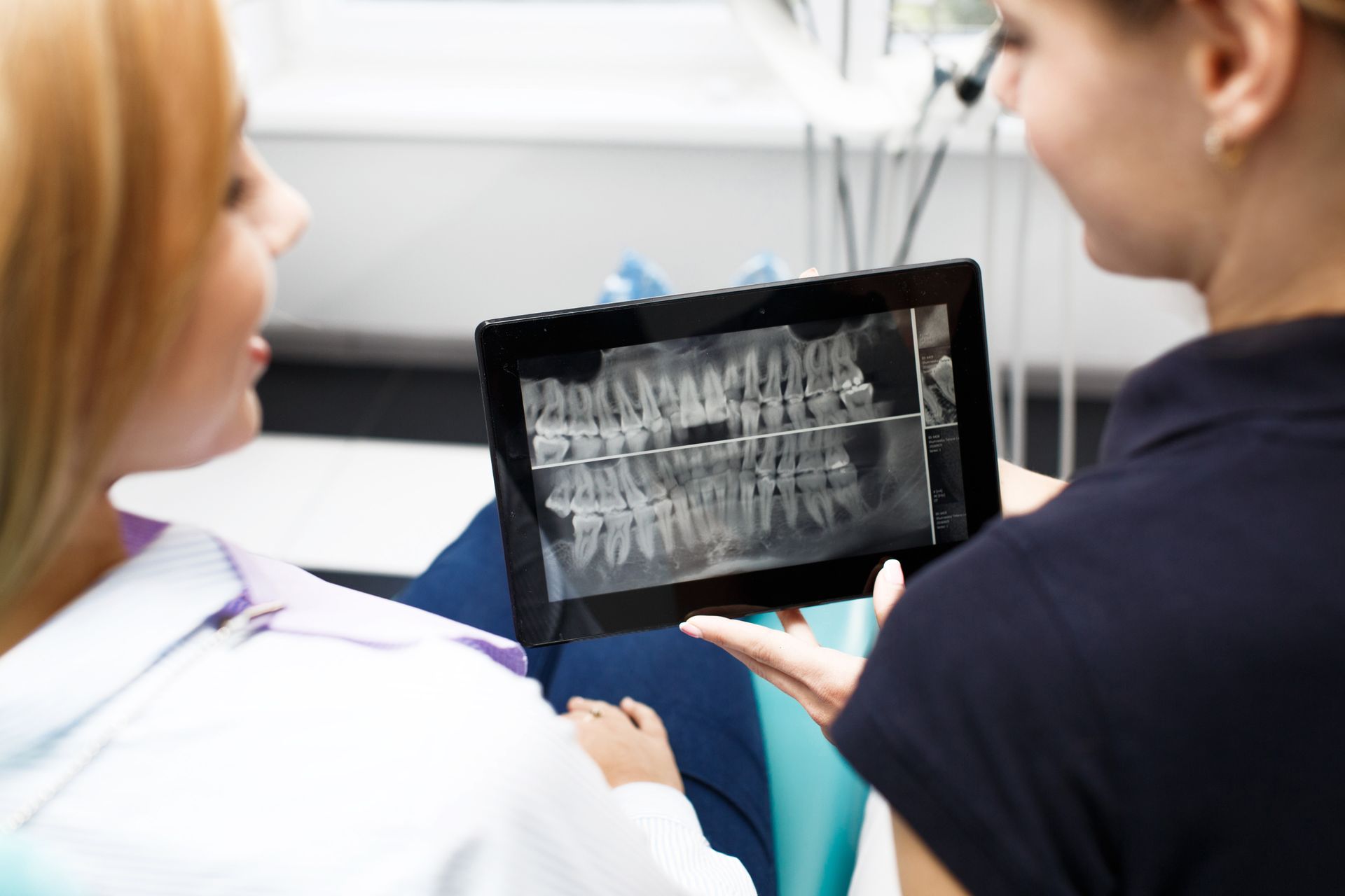 A dentist is looking at an x-ray of a patient 's teeth on a tablet.