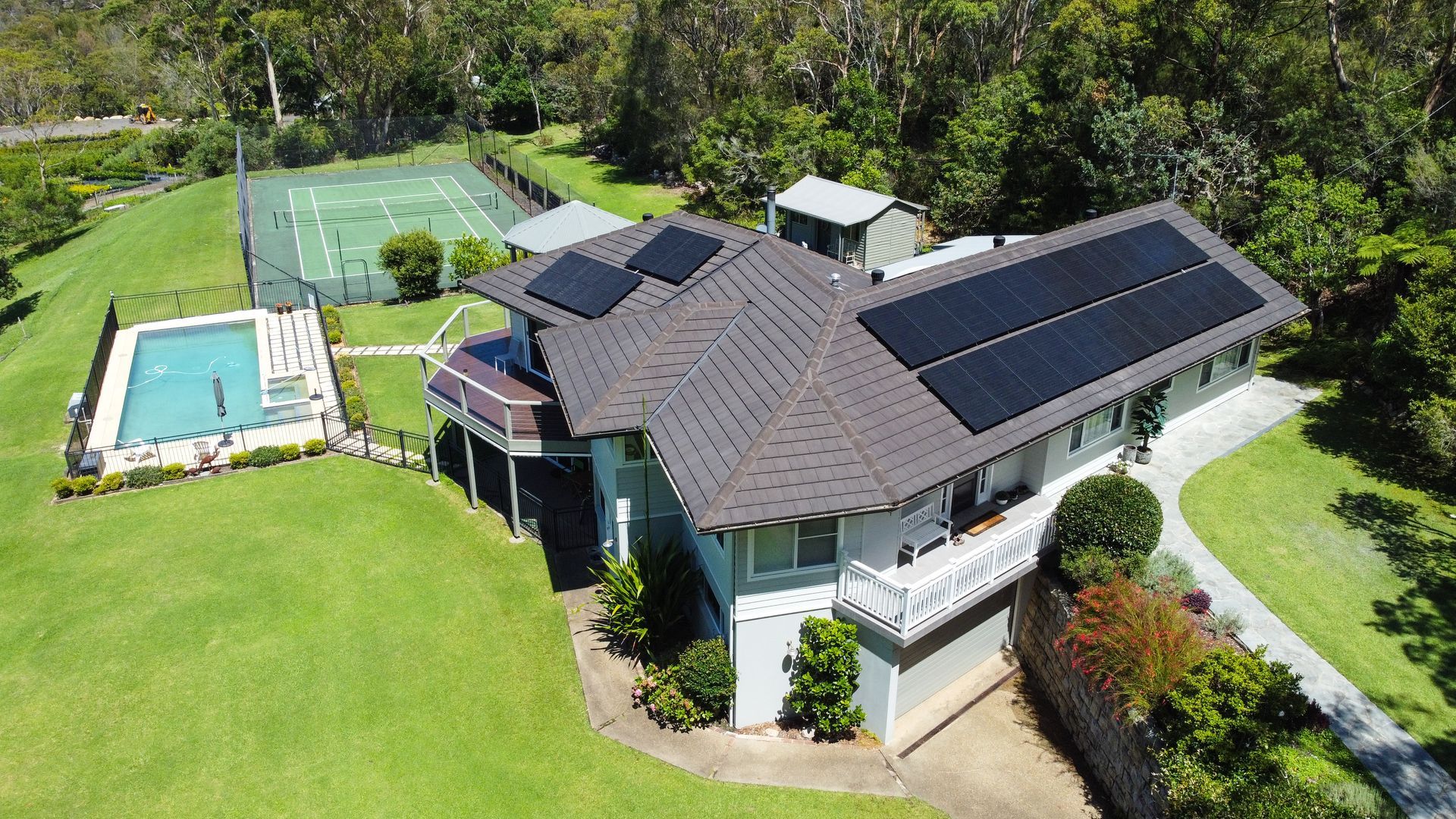 Aerial view of a house with solar panels, a pool, and a large green lawn