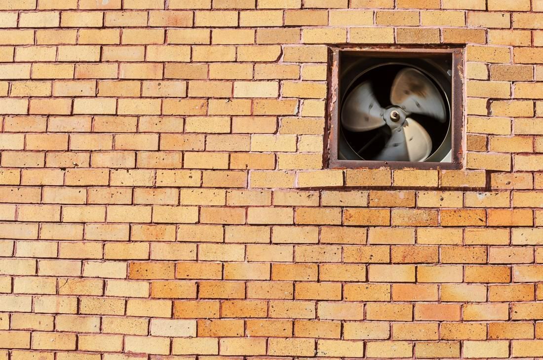 Brick wall with a square opening containing a restaurant kitchen exhaust fan.
