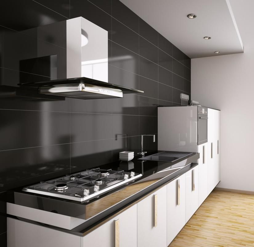 Modern commercial kitchen with black tiled wall, white cabinets, and stainless steel appliances.