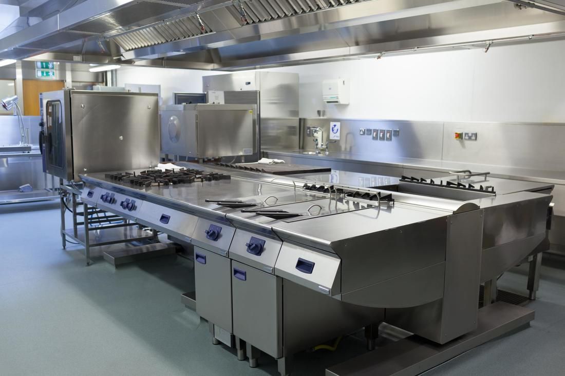 Commercial kitchen with stainless steel appliances, including stovetops, exhaust hood, and cabinets.