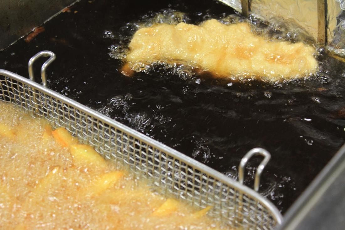 Deep fryer with bubbling oil, fish filet frying, basket of fries.