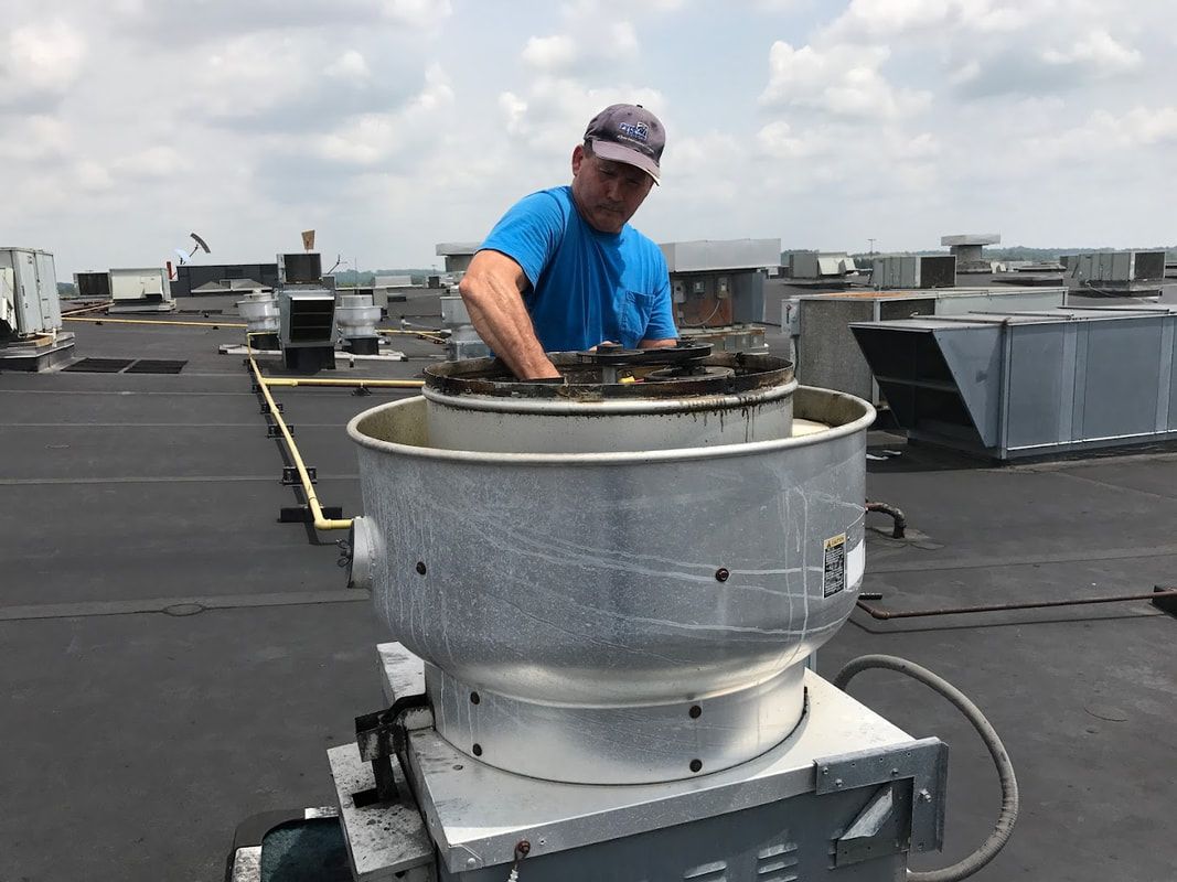 Person in blue shirt working on a rooftop ventilation unit on a flat roof under a cloudy sky.