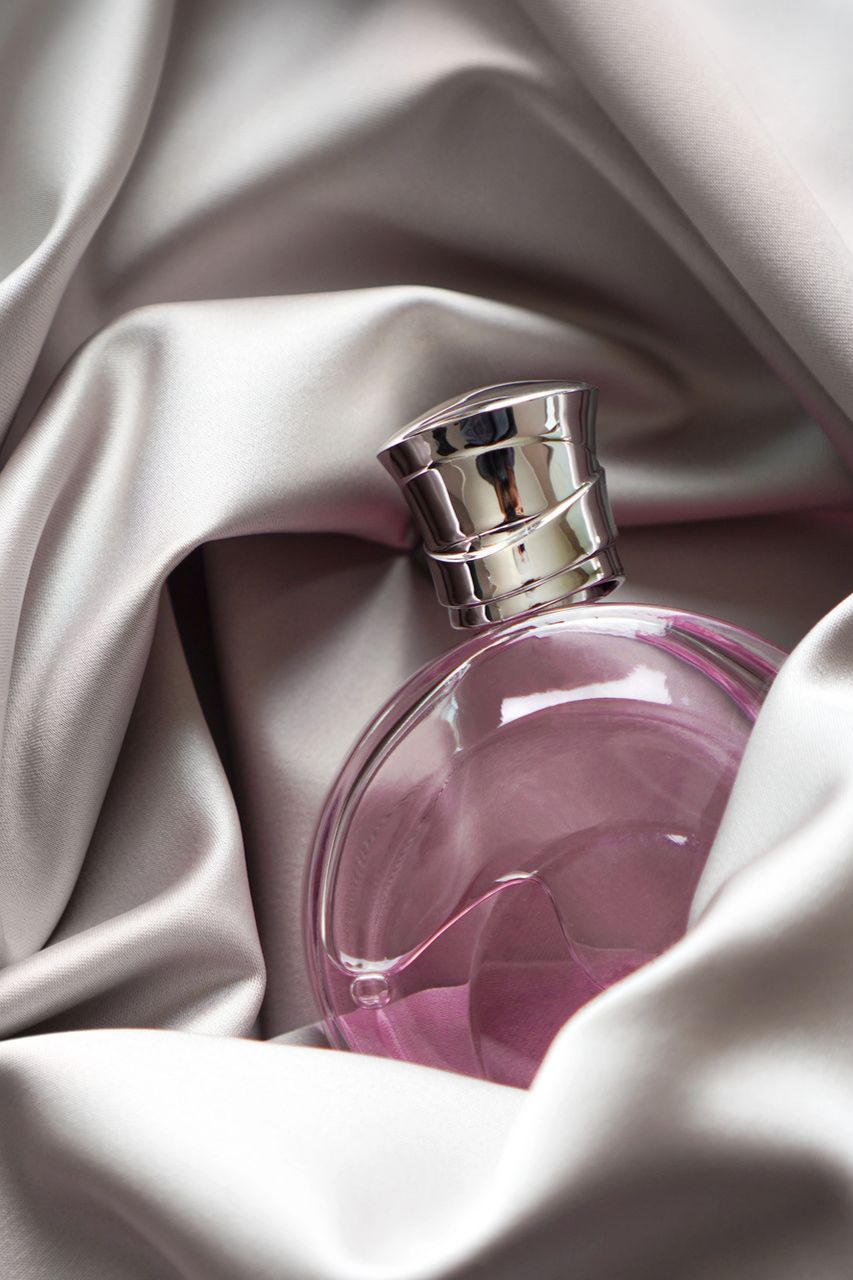 Frasco de perfume rosa sobre tela de satén plateada