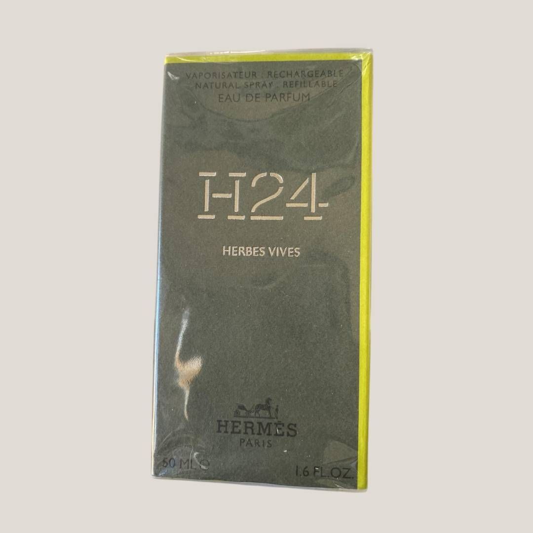 Caja de perfume Hermès H24, verde oscuro con ribete amarillo sobre fondo blanco.