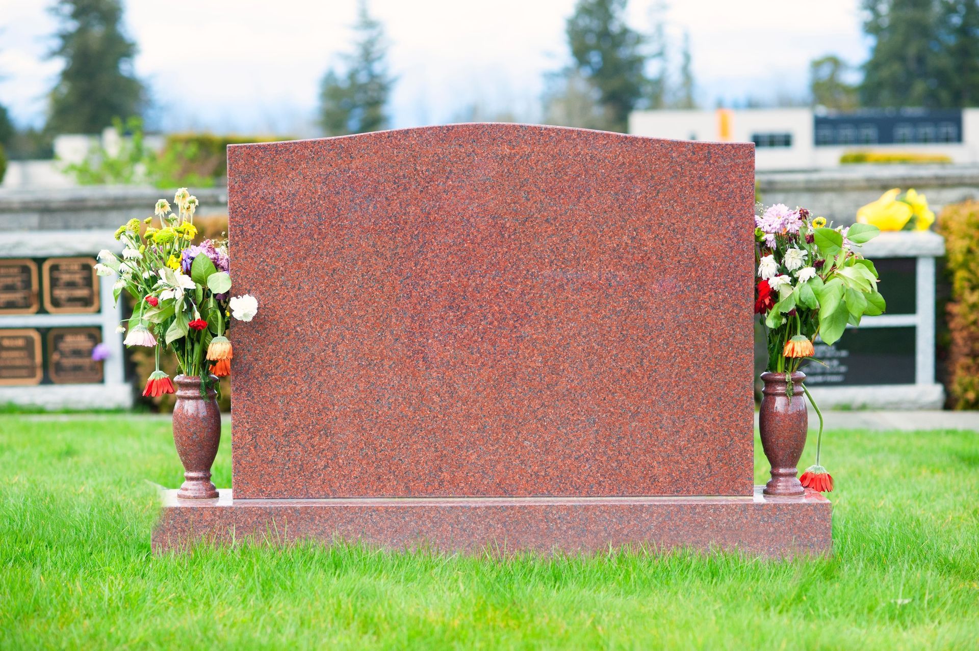 Red granite grave marker with flower vases on a grassy cemetery plot