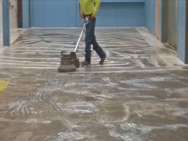 Technician grinding a concrete floor during surface preparation inside a commercial building