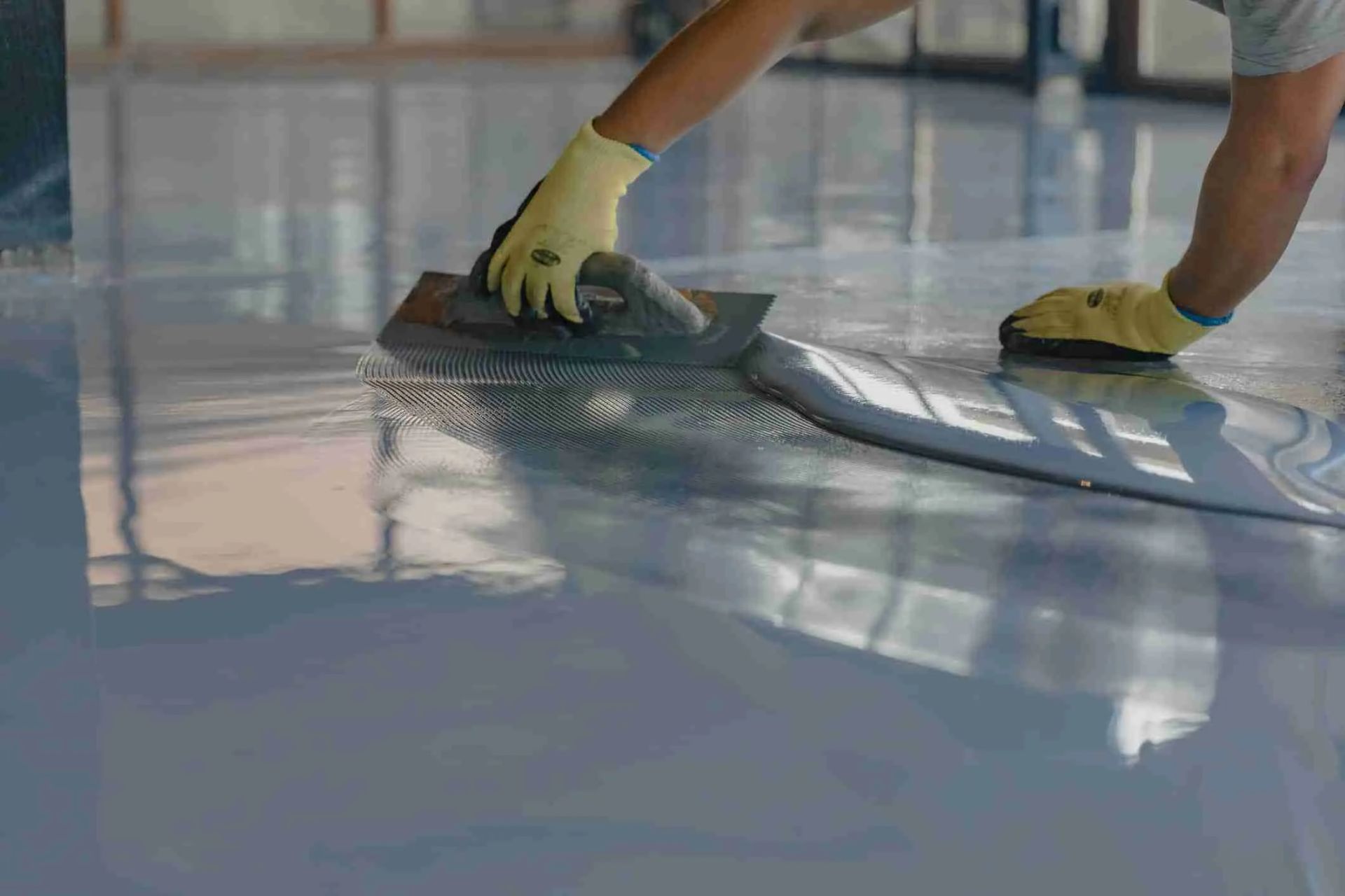 Contractor applying slip-resistant floor coating with a notched trowel on a glossy surface