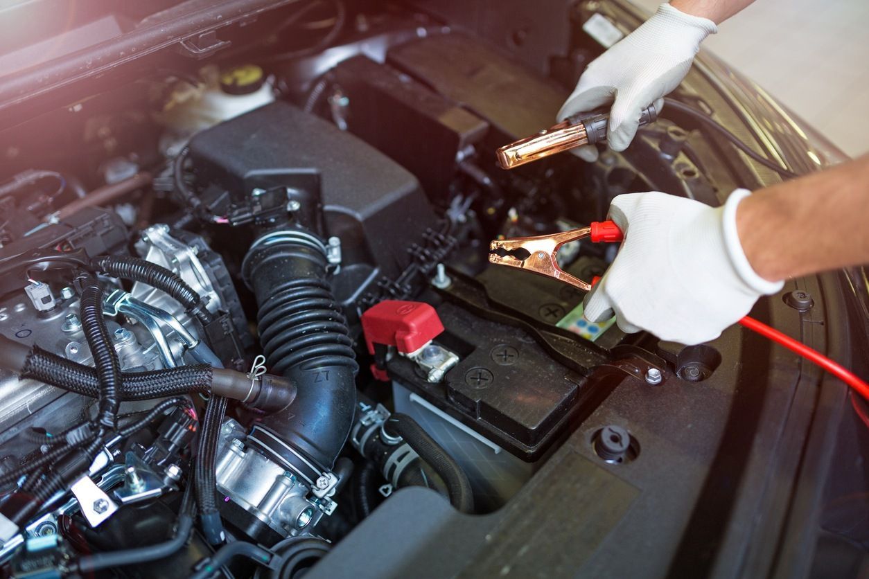 Gloved hands connect jumper cables to a car battery in an open engine bay