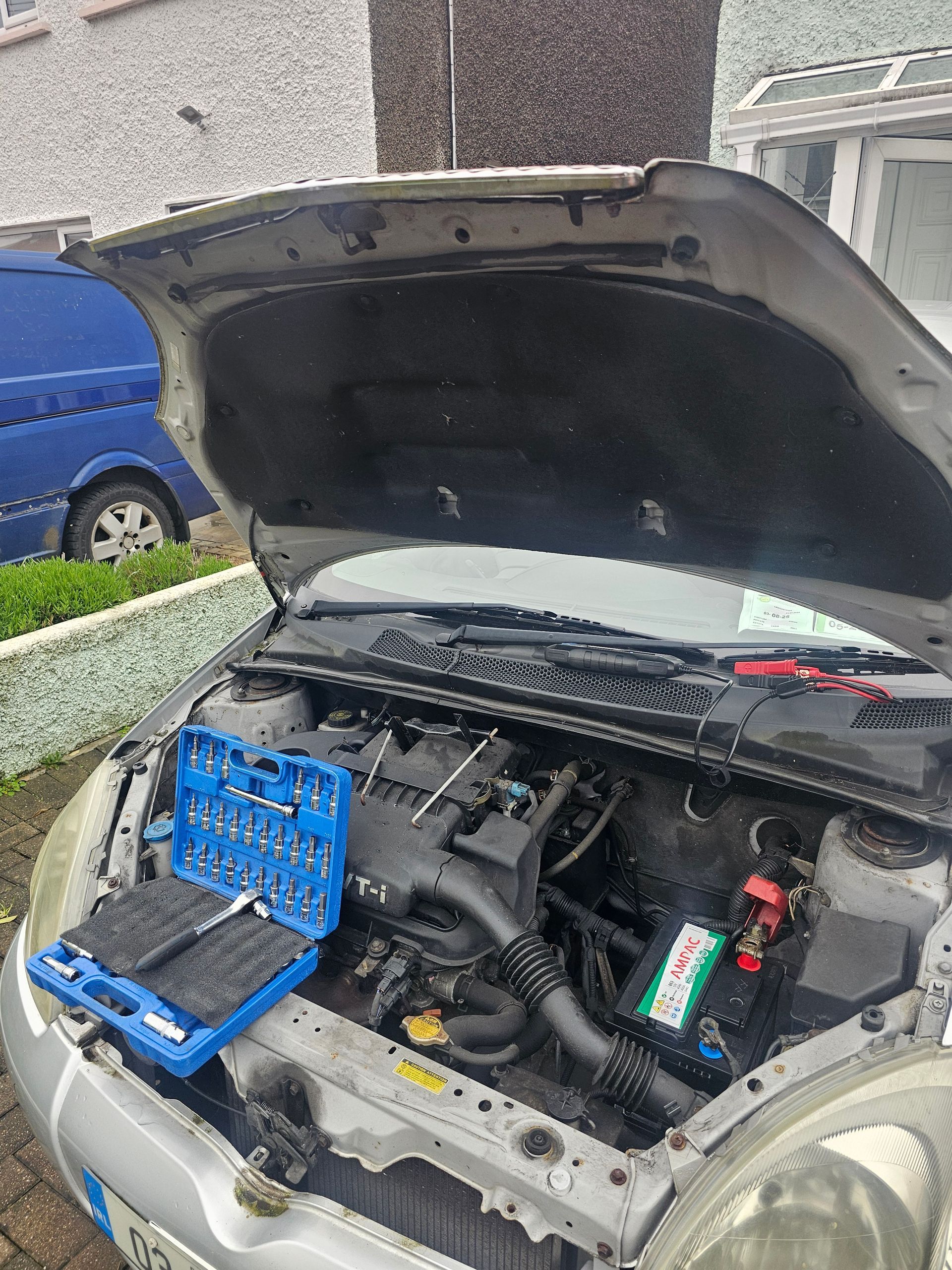 Open car hood with engine exposed and a blue tool case resting in the front compartment