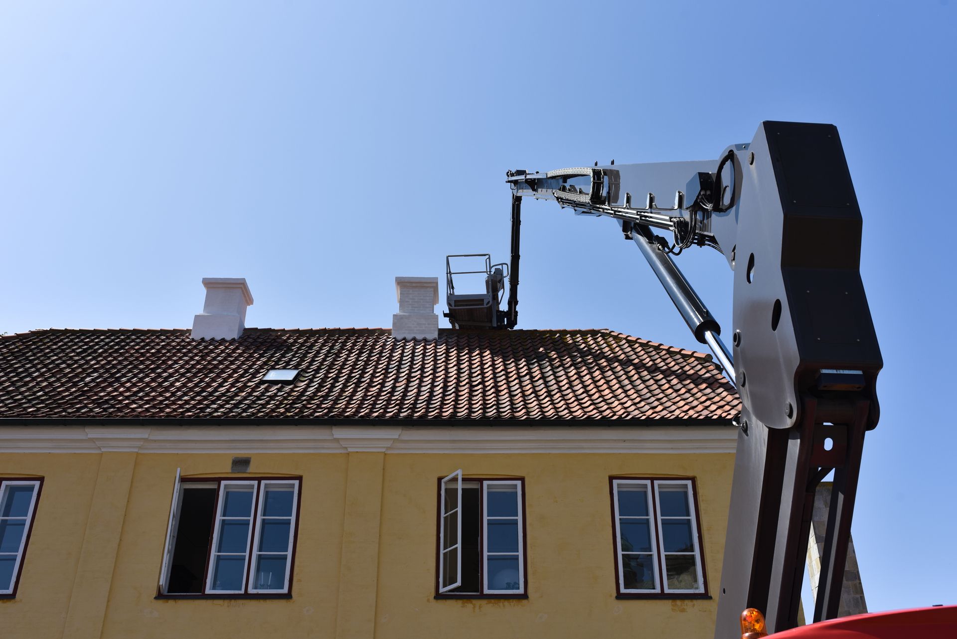 Boom lift raising worker to roof for maintenance on a tiled building exterior. Boom lift raising worker to roof for maintenance on a tiled building exterior.