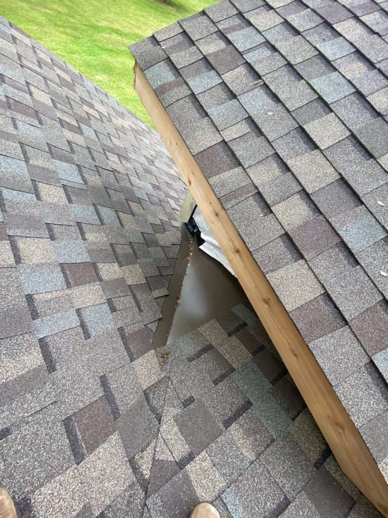 Two roof sections meet, a valley with visible flashing, shingles are brown and gray.