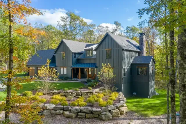 Gray house with stone landscaping surrounded by trees and autumn foliage