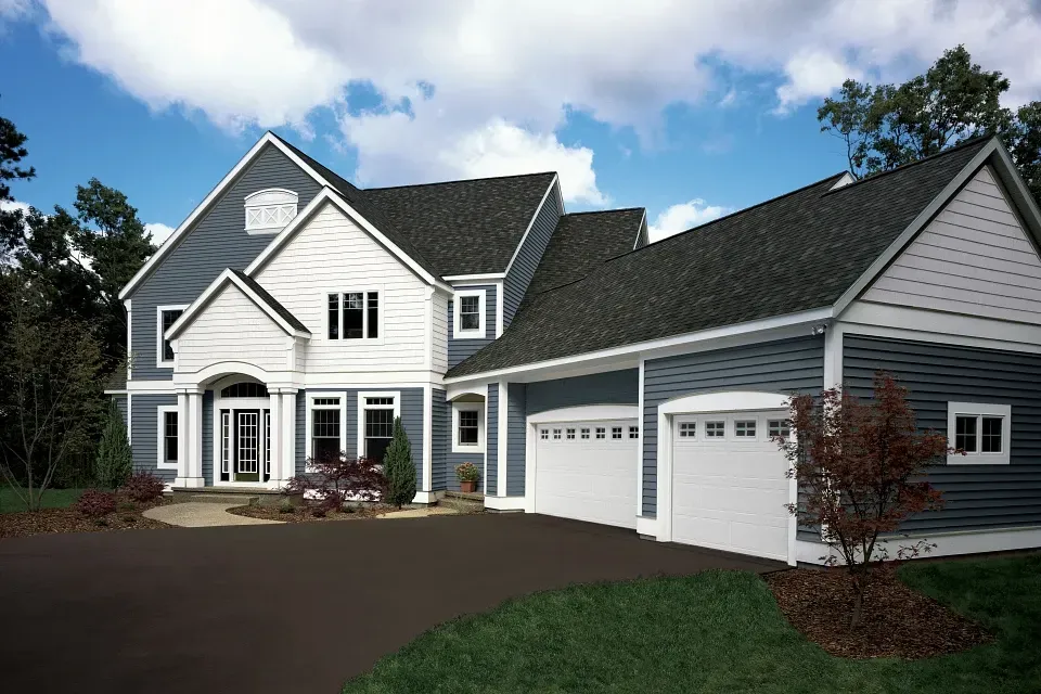 Large gray suburban house with white trim and a three-car garage under a partly cloudy sky