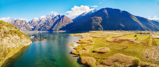 Una scena di lago con montagne sullo sfondo e un'area erbosa in primo piano sotto un cielo azzurro.