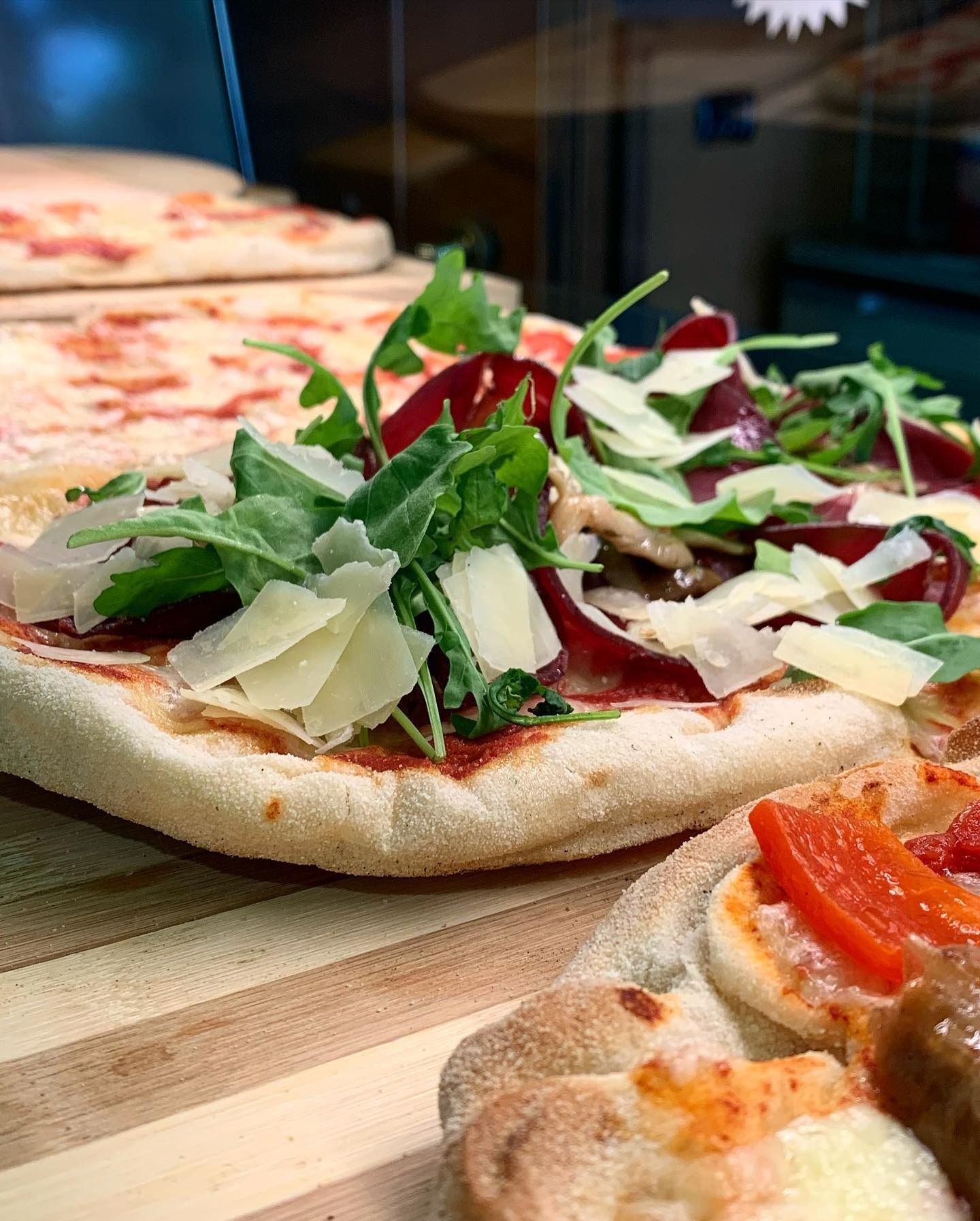 Primo piano di una pizza condita con rucola, parmigiano grattugiato e carne.