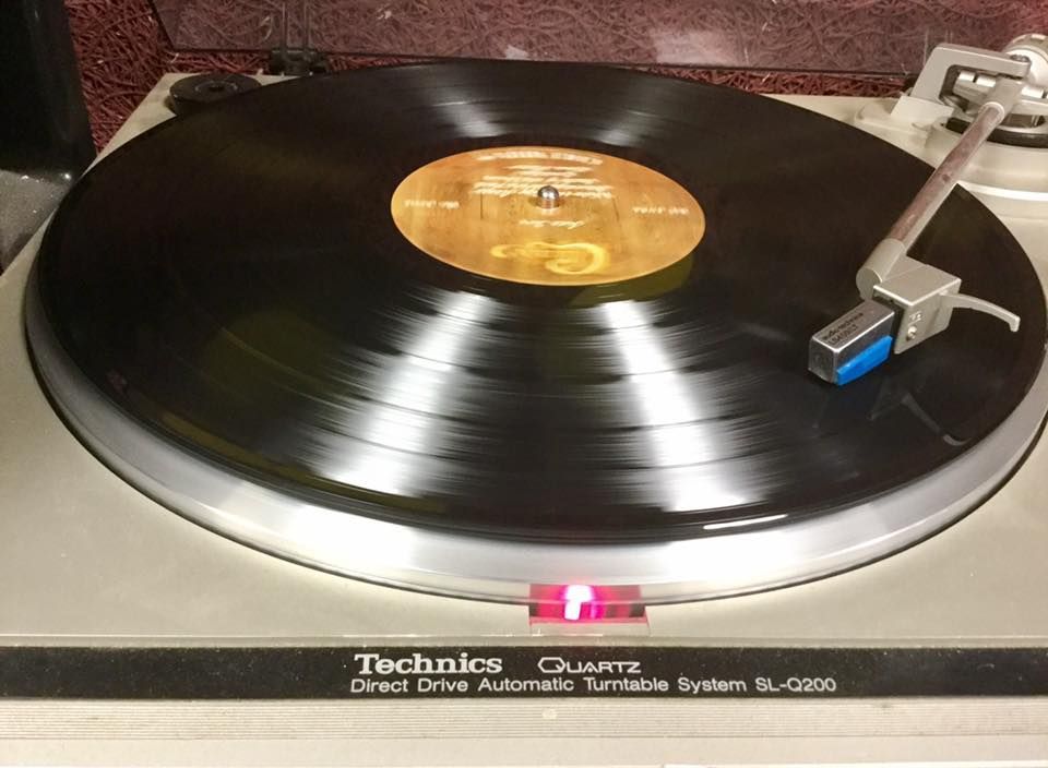 Technics turntable playing a black vinyl record with a gold center label and tonearm at right