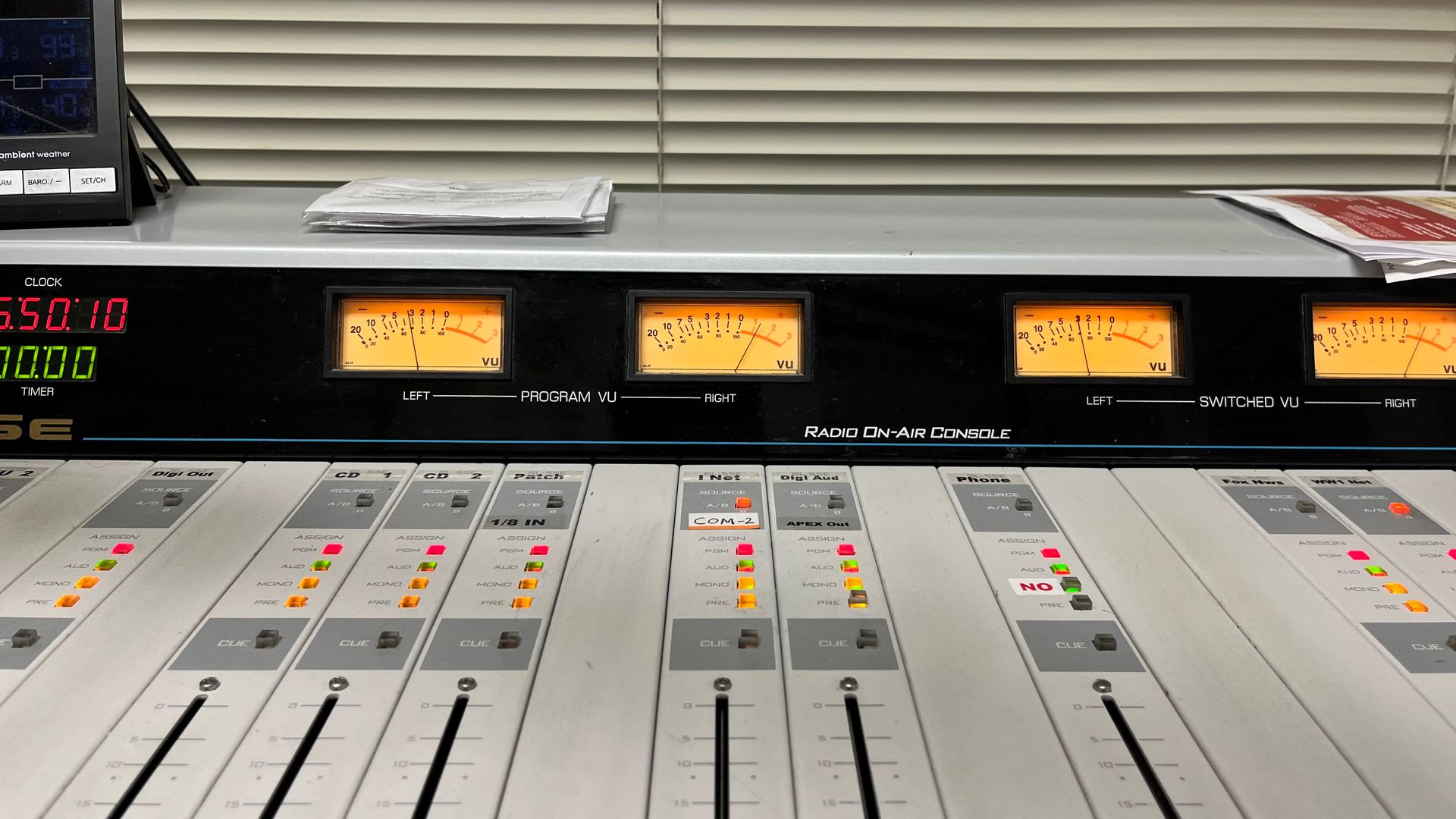 Radio mixing console with sliders, meters, and illuminated control panels in a studio.