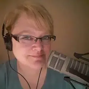Woman with glasses and headphones speaks into a microphone; close-up shot.