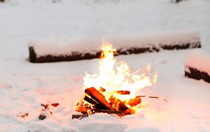 Small campfire burning on snow-covered ground with a log bench in the background