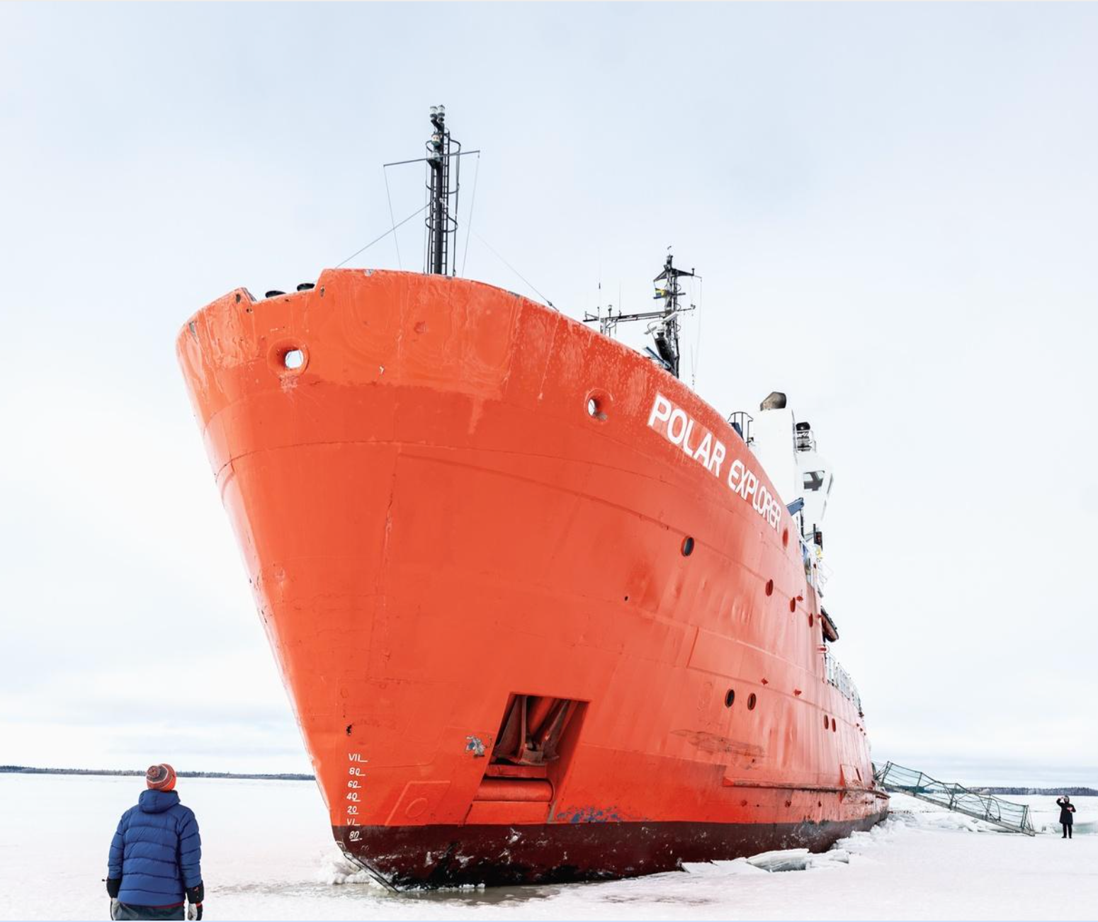 Orange ship stranded in snowy landscape with a person standing nearby
