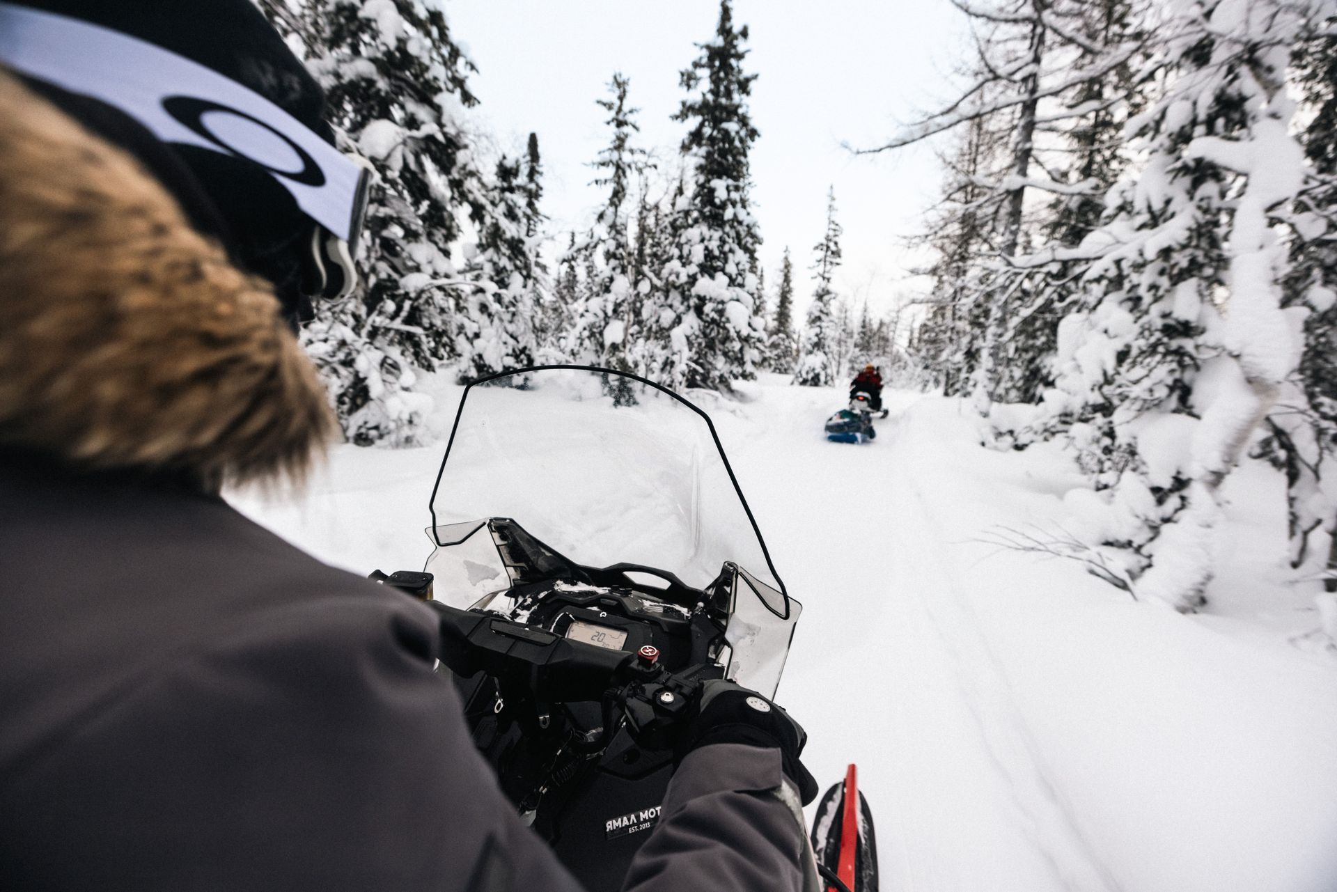 Snowmobile rider in a snowy forest trail following another rider ahead
