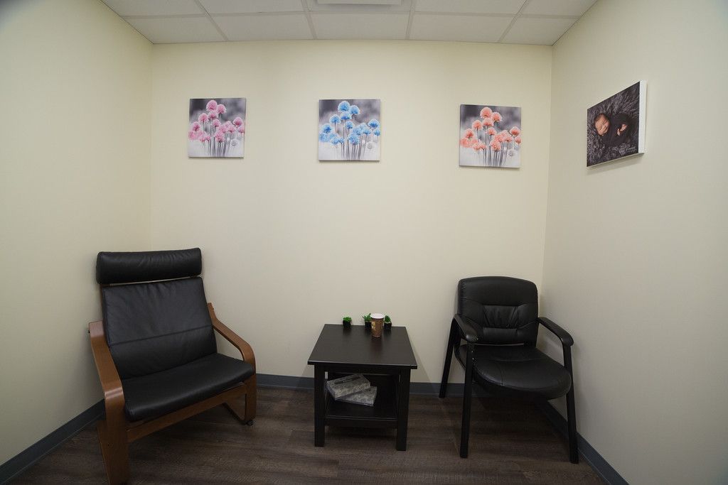 A counseling room with two black chairs, a small table, and three floral paintings on the wall.