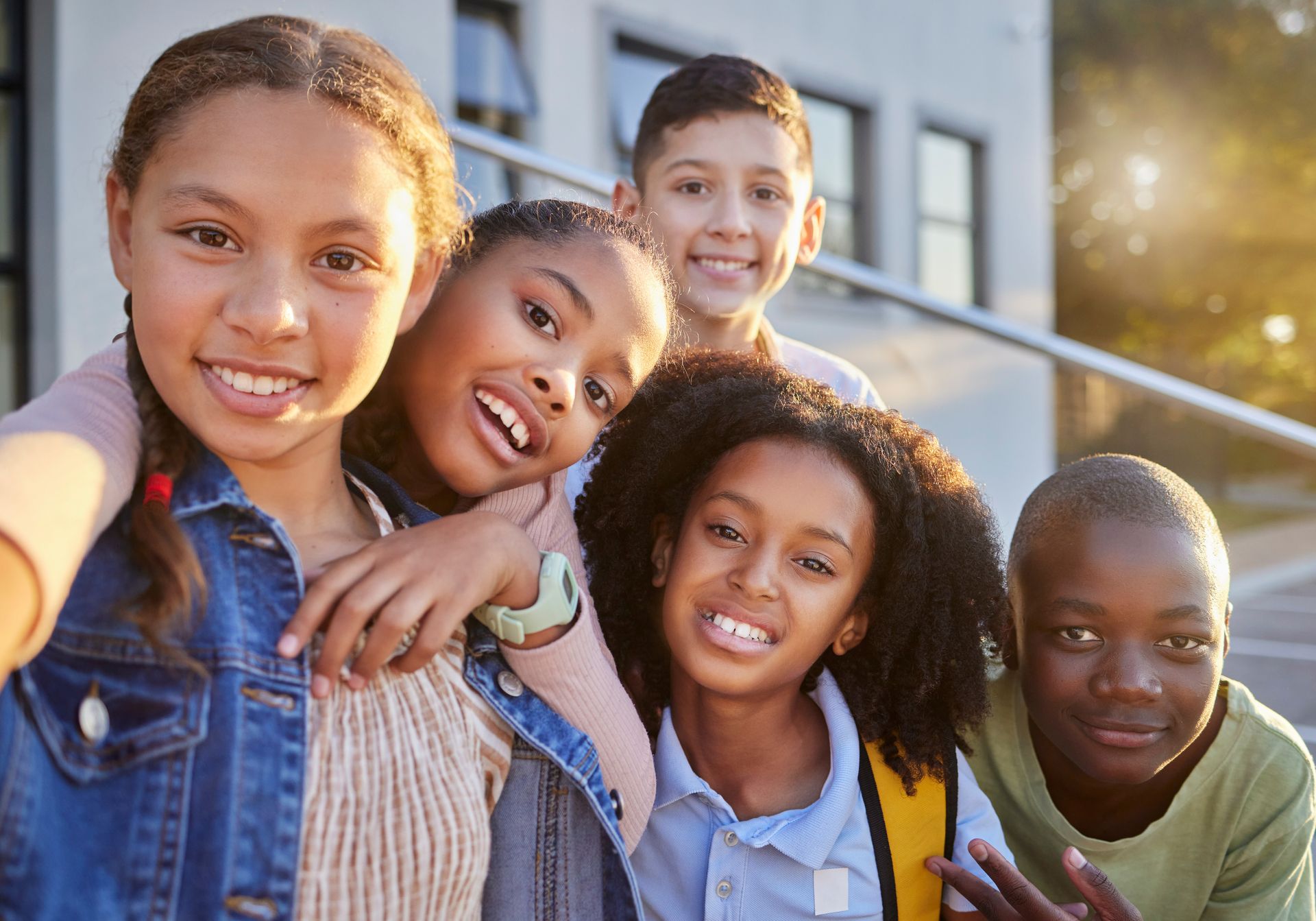 Five smiling friends posing outdoors in front of a building, one taking a selfie