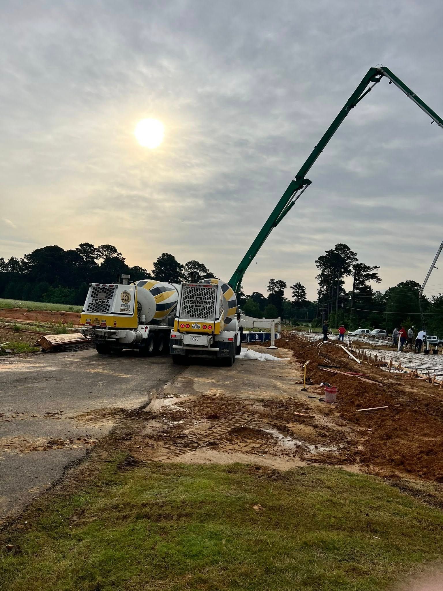 Two concrete trucks and a pump pouring concrete on a construction site, under cloudy sky.