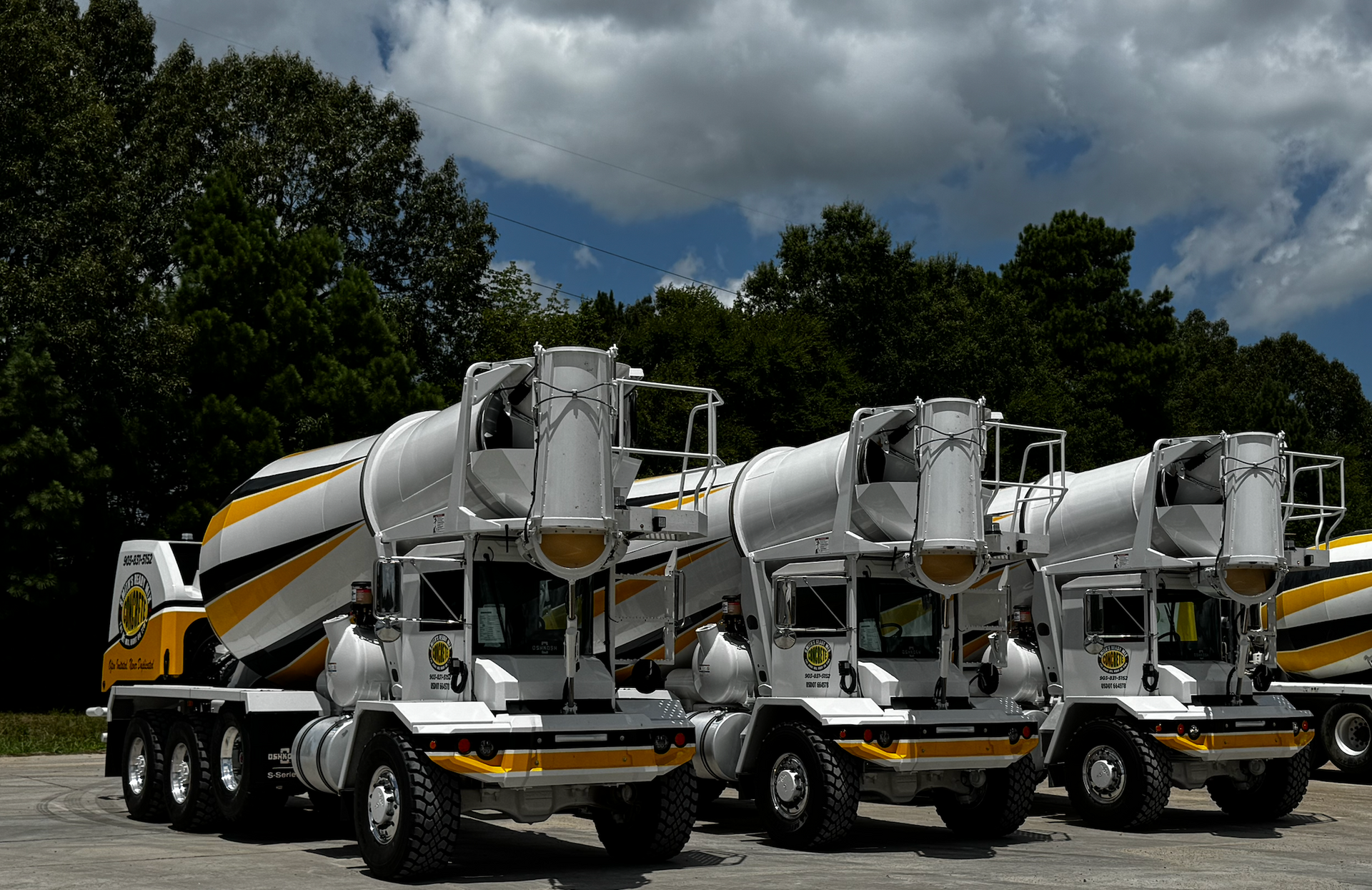 Three yellow and white concrete mixer trucks parked outdoors.