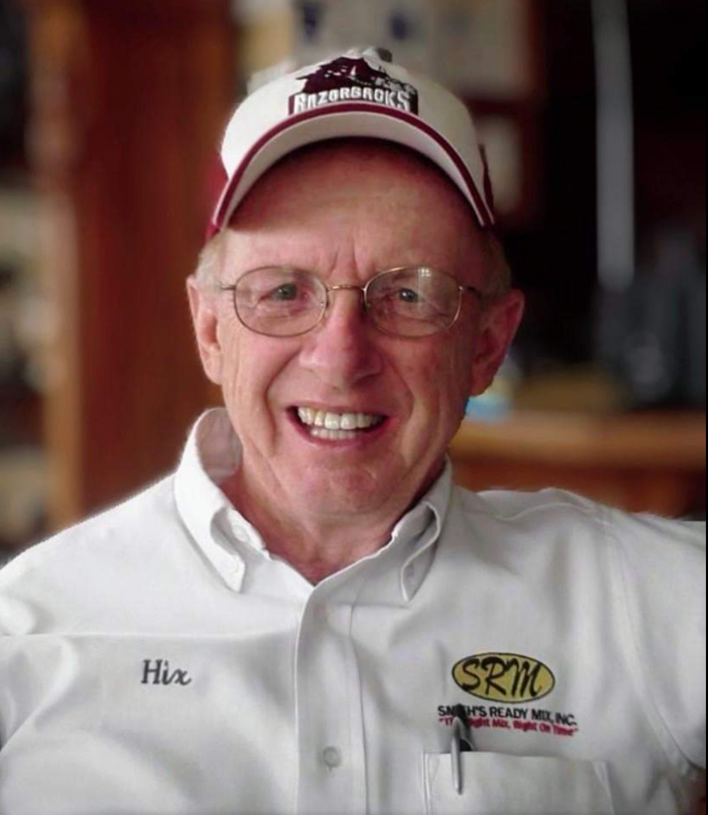 Smiling elderly man wearing a baseball cap and glasses, with a white shirt.