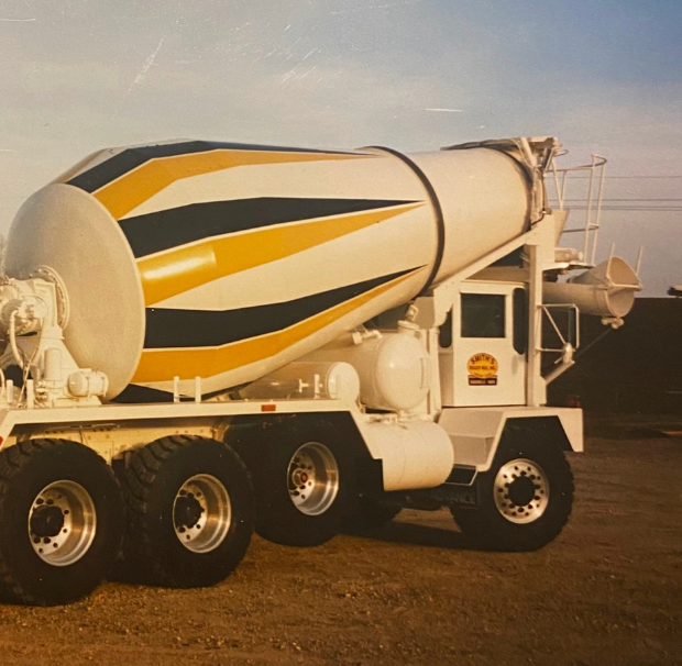 Cement truck, white with yellow and blue stripes, on a construction site.