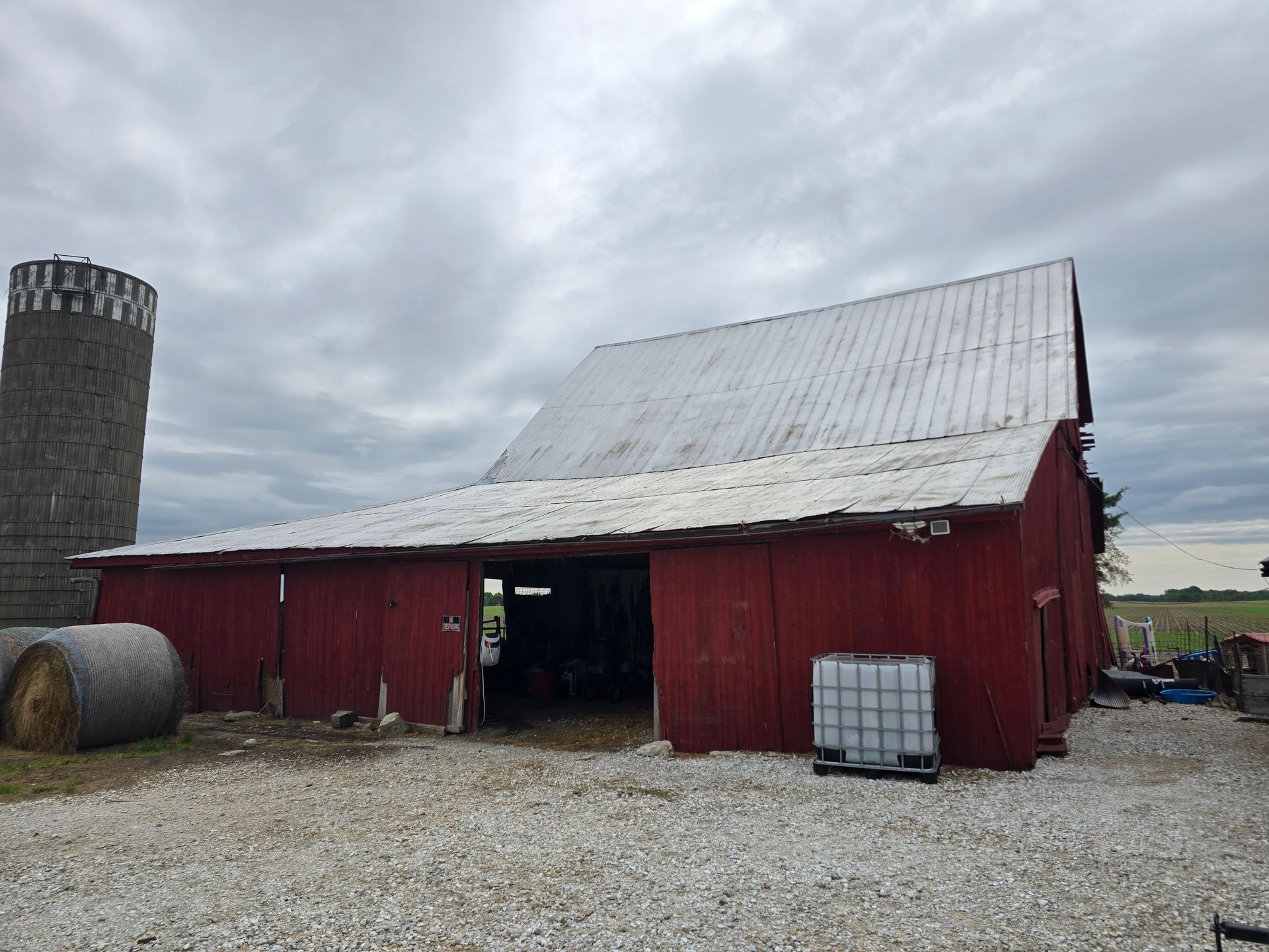 Red barn with white metal roof on a gravel farmyard under a cloudy sky