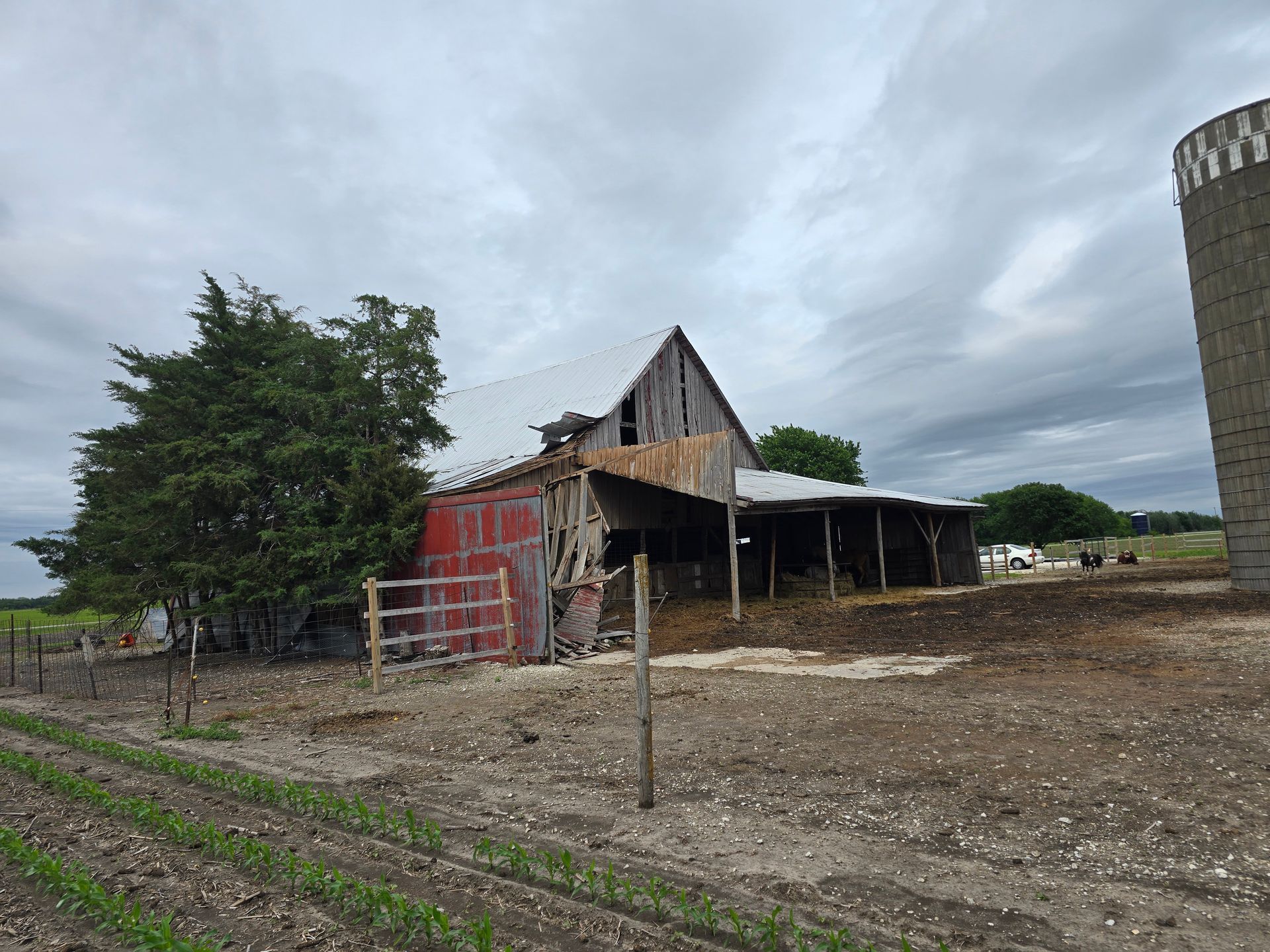 Old red barn beside a dirt field under a cloudy sky, with a silo on the right.