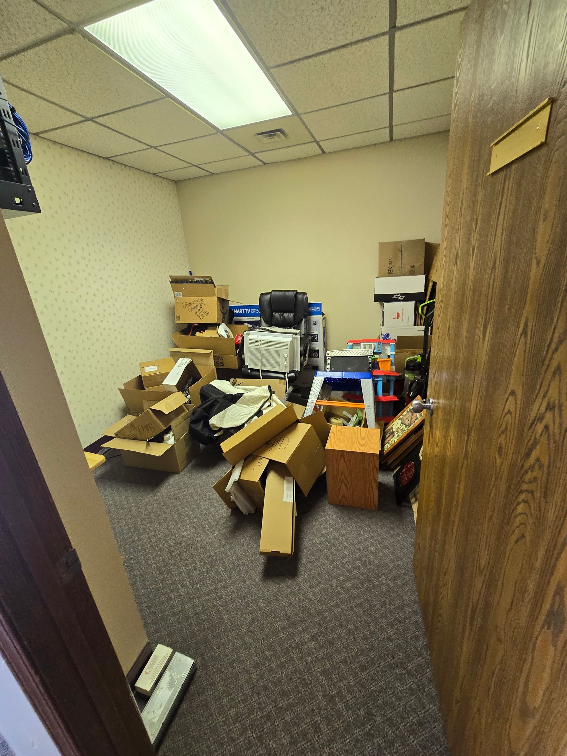Cluttered office with stacked cardboard boxes and scattered packing materials on the floor.