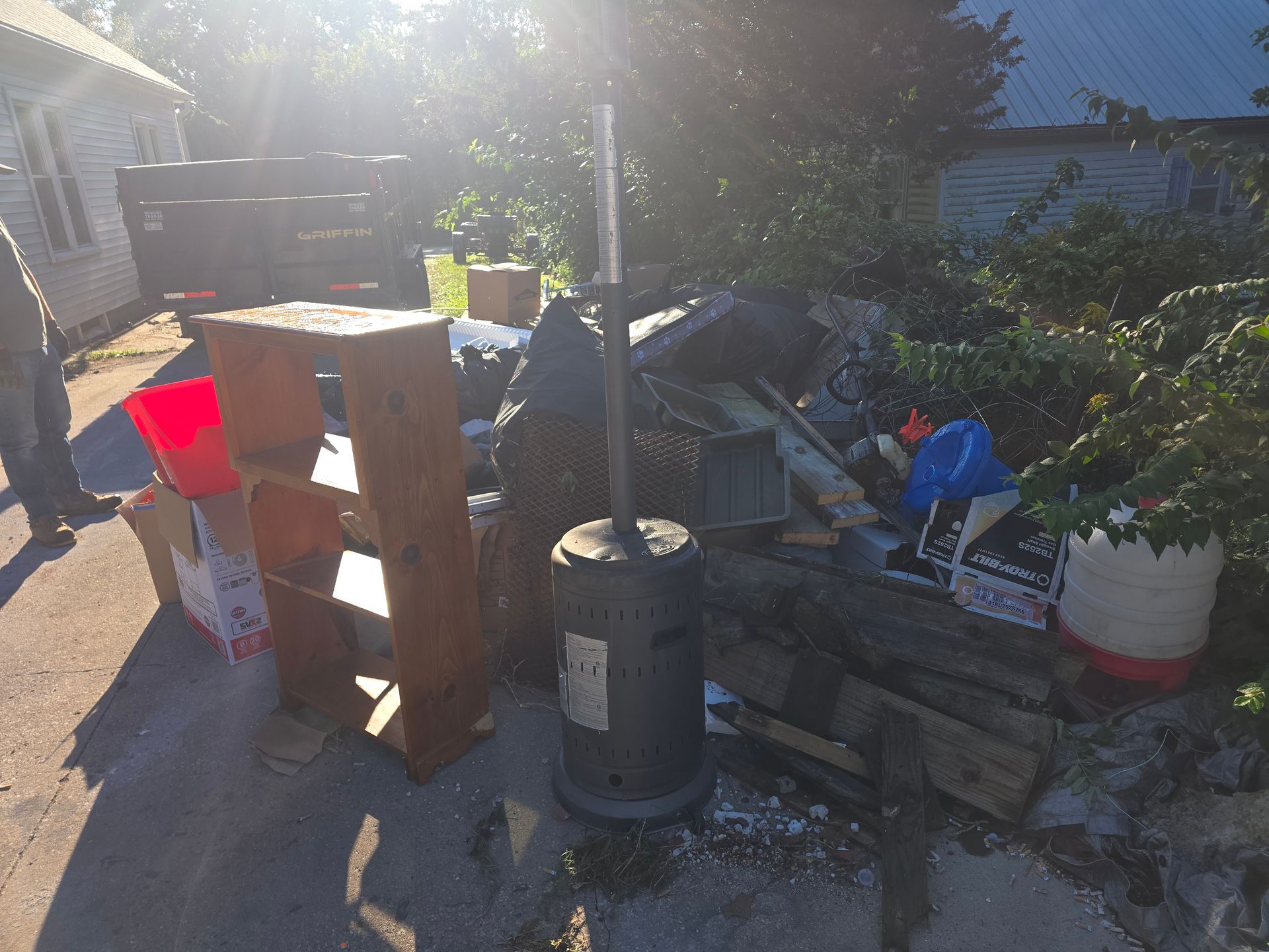 Backyard with stacked bricks, wooden pallets, a heater, plants, and scattered garden items in bright sunlight