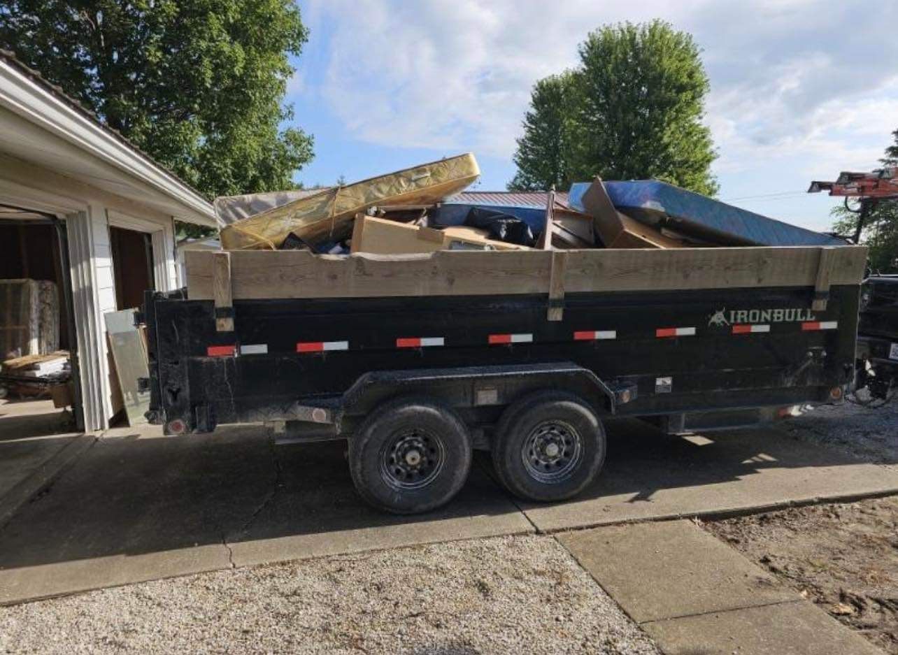 A dumpster trailer filled with junk is parked in front of a house.