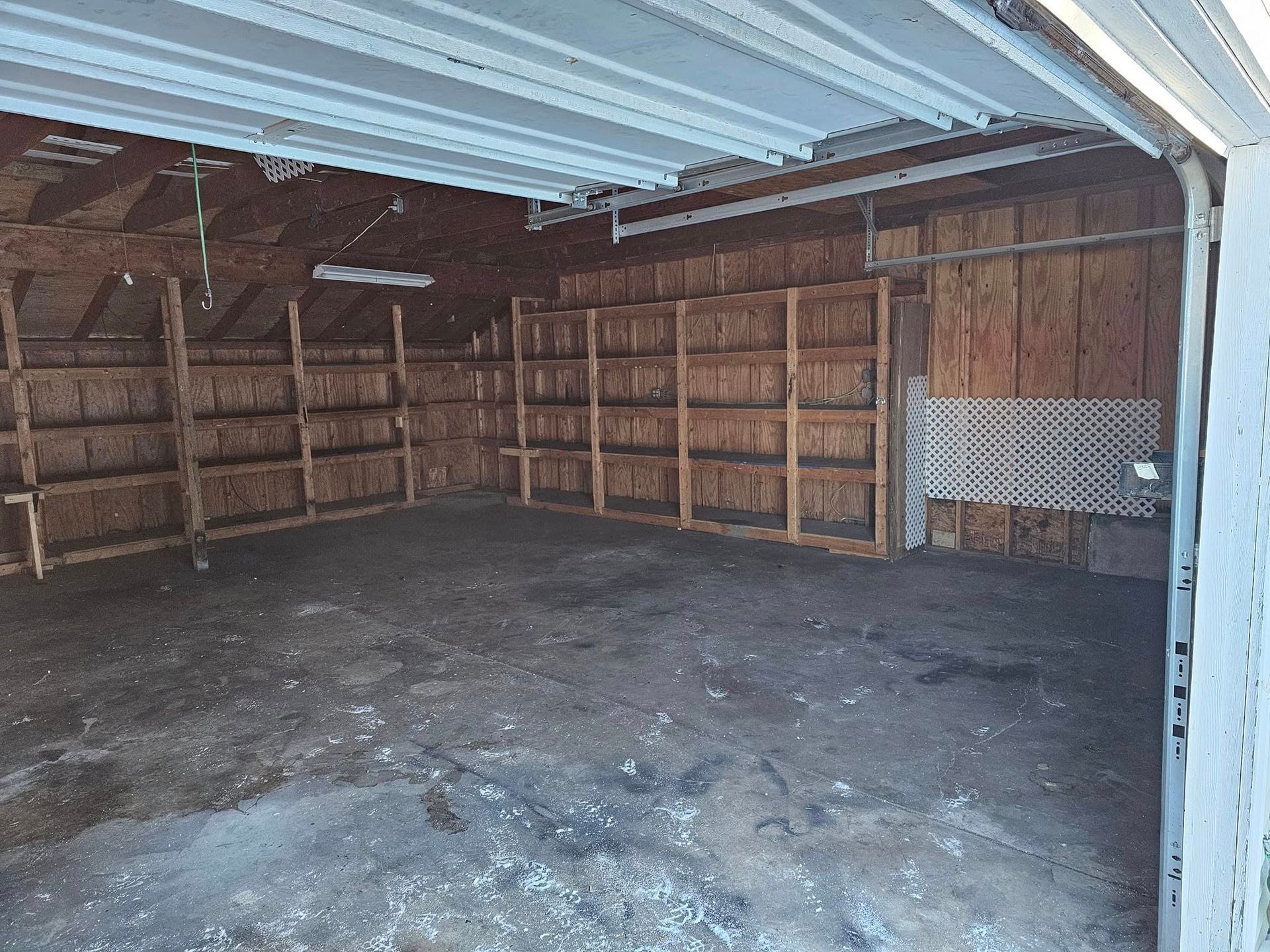 An empty garage with a garage door open and shelves.