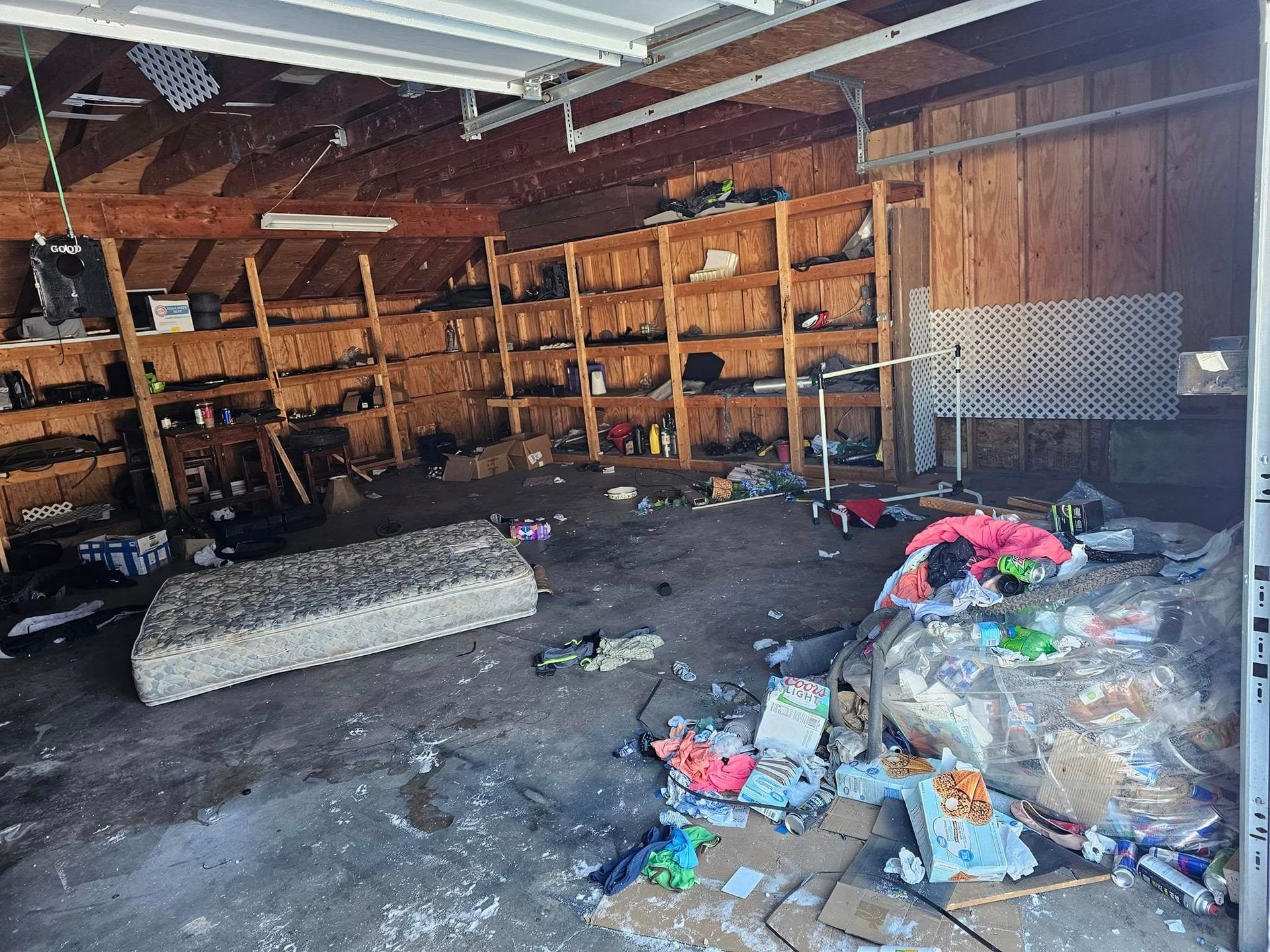 A garage filled with lots of junk and a mattress on the floor.