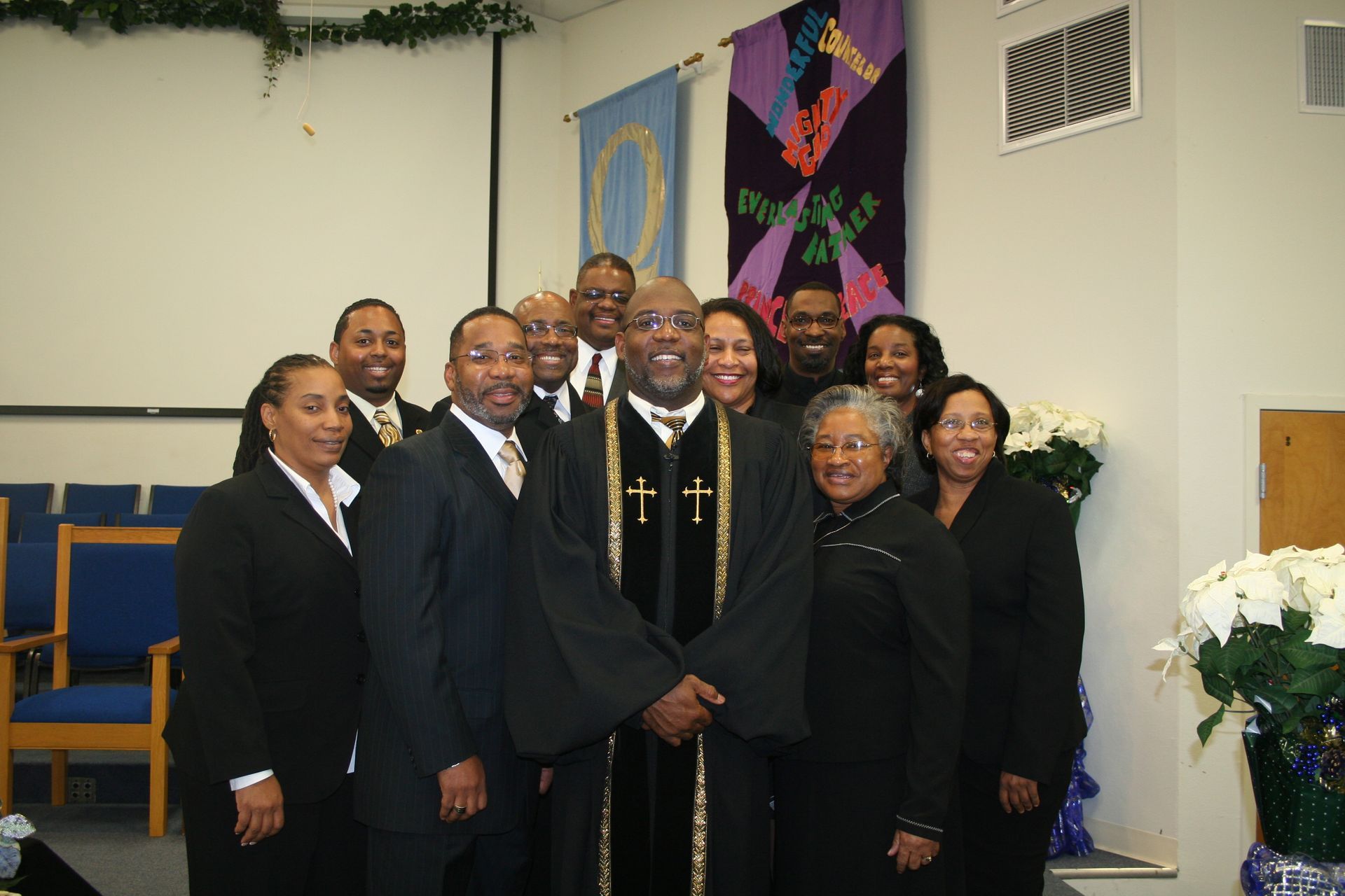 Group of people in black formal attire posing indoors near church decorations and flowers.