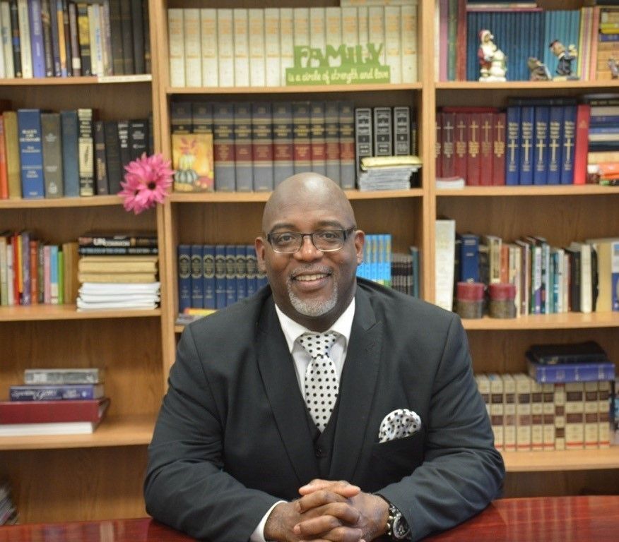 Man in suit, smiling, in front of a bookshelf filled with books,