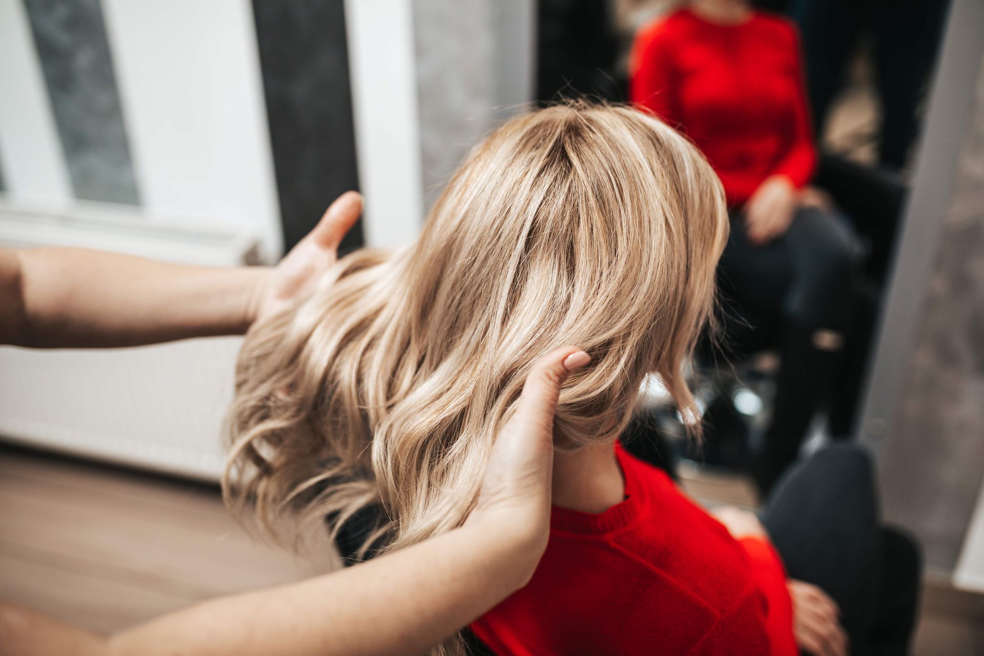 Person with blonde wavy hair in red top being styled by hands.