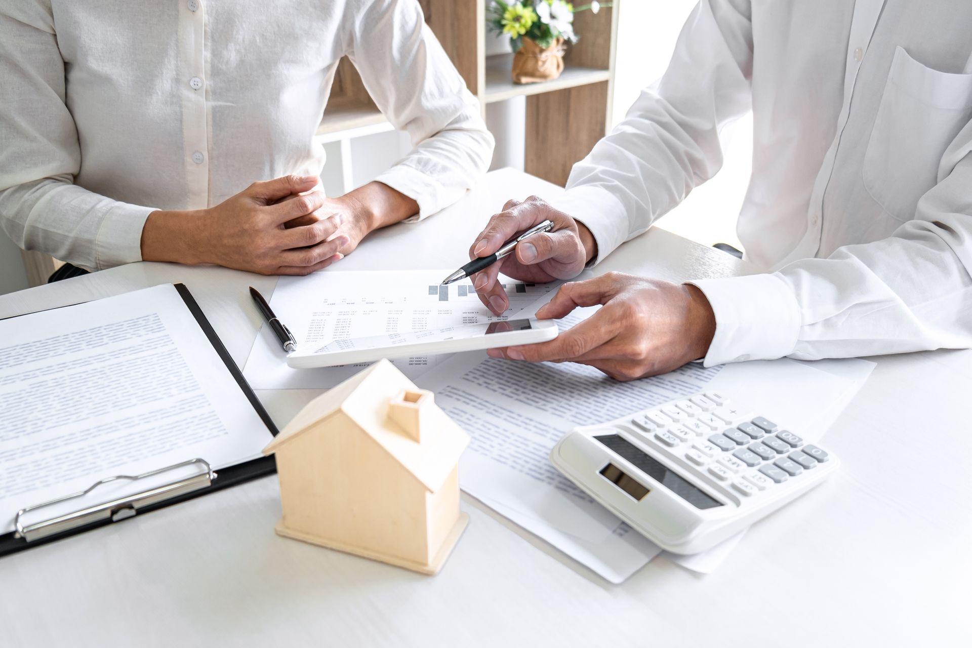 Two people reviewing documents beside a calculator and small house model at a desk