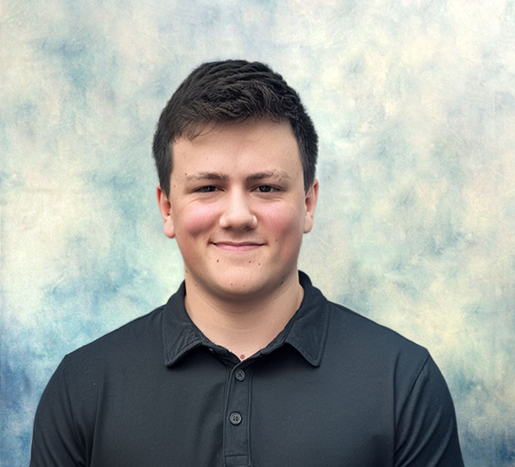 Portrait of a smiling man in a dark shirt against a softly blurred pastel background