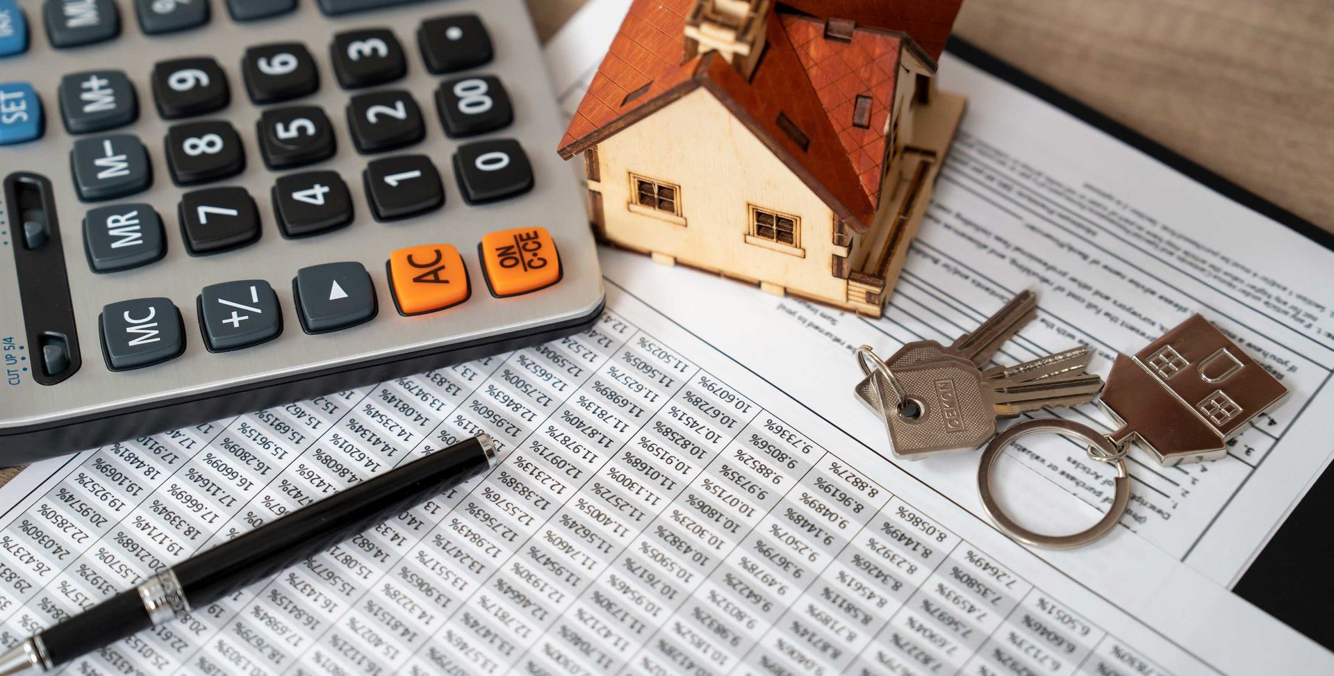 Calculator, house model, keys, pen, and paperwork on a desk, suggesting home finances or property documents