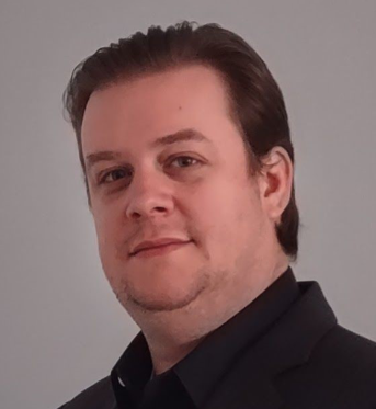 Portrait of a person in a black blazer against a light gray background, looking at the camera with a slight smile.