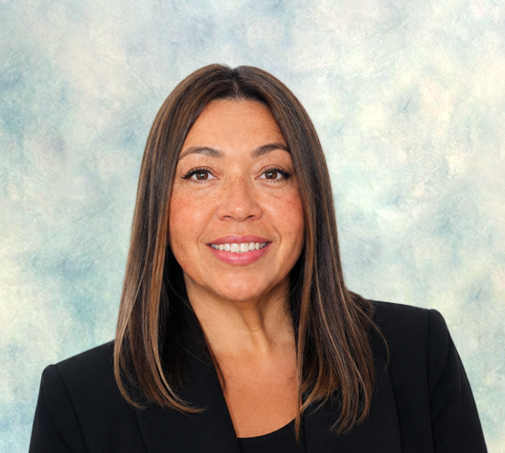 Portrait of a smiling person in a black blazer against a soft blue-gray backdrop