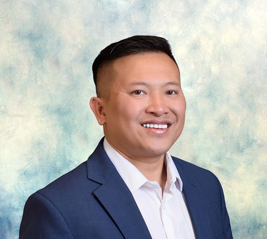 Smiling man in a navy suit and white shirt against a light blue studio backdrop