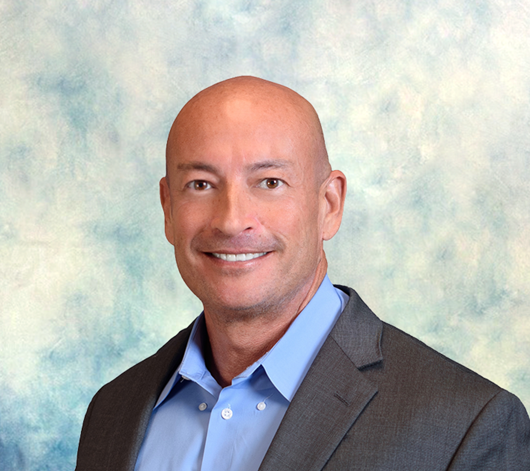 Smiling bald man in a dark blazer and blue shirt against a soft pastel backdrop