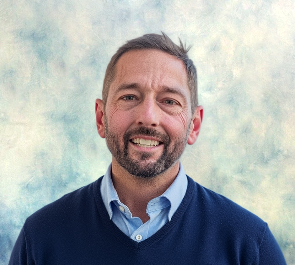 Smiling man in a navy sweater and blue shirt against a softly blurred light background